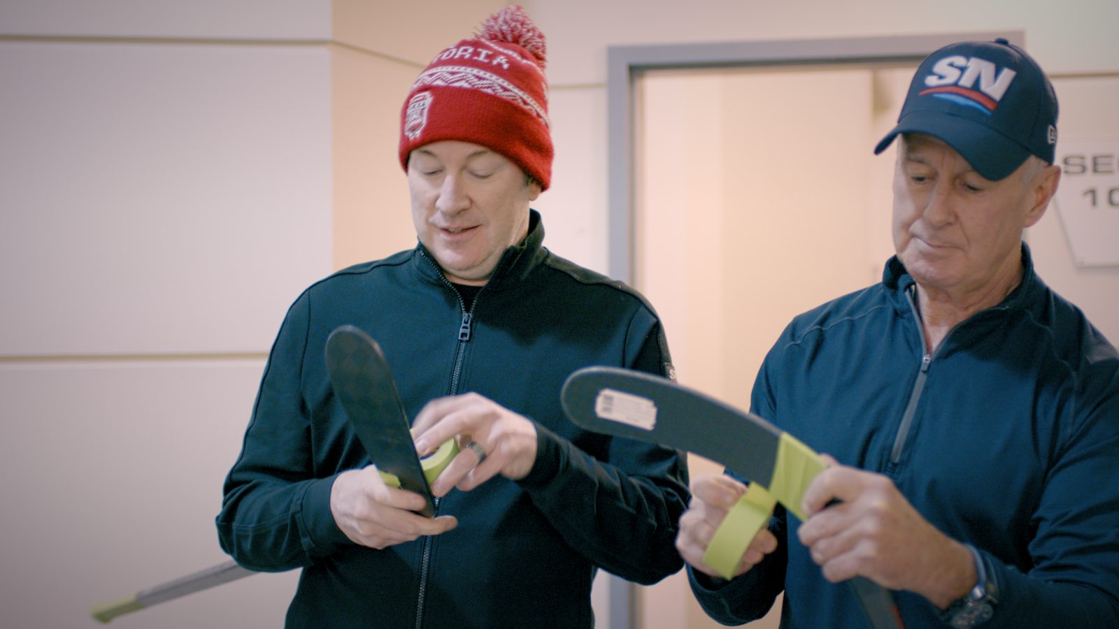 Two coaches inspecting the green tape on a stick blade